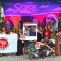 A group of YES alumni and staff pose with YES program flag and banner frame in front of a vibrant mural featuring Mother Teresa