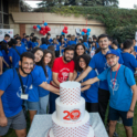 A Group Of Alumni Cutting A Cake With The 20Th Anniversary Logo