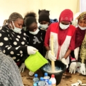 A group of participants gathered around a table wearing gloves and masks as they pour liquid from a green container into a large black bucket