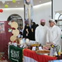 A group of young people standing at a table of food with the Saudi flag