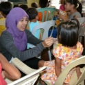 A Woman Feeding A Young Girl Sitting On A Plastic Chair