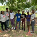 Alumni and volunteers pose outside hold rakes