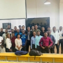 Alumnus posing with group of students in front of lecture hall