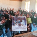 Group of students with their hands in the air. Students at the front are holding a Girls and Science poster.