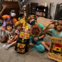 YES student sitting with a group of young children holding up traditional Ghanian clothes and decorations.