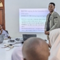 Grantee Alfred in front of presentation leading a STEM discussion with participants seated around him