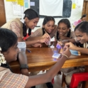 Group of female students working on a circuit making the a LED light glow using a breadboard wires and a battery