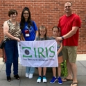 A family of three stands with Hind holding an IRIS flag