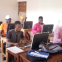 Nine people sit behind computers. They focus on the screens. 