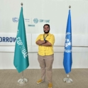Idriss standing in between a COP28 UAE flag and a UN flag