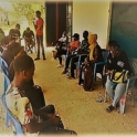 Group of people sitting outside in chairs with Hassan walking and talking with people as a facilitator.