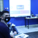 YES alumnus wearing a mask looks at a screen that displays a "Kahoot" game on the projector about first aid