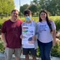 Male teen with two host family members holding welcome signs