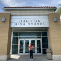 YES student standing outside a school with the sign "Hugoton High School"