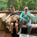 Mert sitting with host mom, smiling, each holding a dog