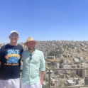 Mohanad and James smile and pose together in front of a blue sky and view of Amman