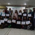 A group of participants standing in a semicircle, holding up workshop certificates
