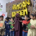 Pakistan A group of young boys standing together and smiling with a woman in the center who is wearing a purple niqab and is interacting with them Behind them golden balloon letters spell RAMADAN KAREEM