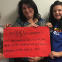 YES alumna standing next to her host family holding up a red sign that reads "The heart of a volunteer is not measured by size, but by the depth of the commitment to make a difference in the lives of others."