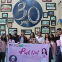 Alumni stand in front of a wall holding up a sign that says "pink out"