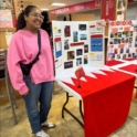 Sama in a pink sweater standing next to a poster display about Bahrain