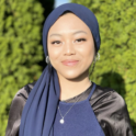 Dinda smiling at the camera in a portrait with a blue hijab