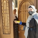Shahed smiling and giving cookies to a neighbor as they open the door. 