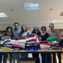 Six Alumni With Piles Of Folded Clothes On Table In Front Of Them