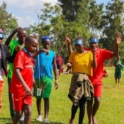 Six children participating in a outdoor activity all holding and balacing a cup tied with strings to each one of the team