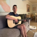 Mert Ozer from Turkiye sitting on a couch holding a guitar