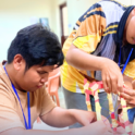 Three young participants are engaged in a hands on group activity focusing intently on building a structure out of materials