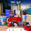 Three Young People Standing With A Stack Of Boxes And Bags Of Donations With A Ladybird School Sign