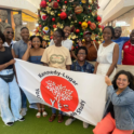 Group photo smiling in front of a Christmas tree, holding up a YES flag