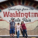 YES student standing with her host parents in front of a sign that says "Greeting from the Washington State Fair"