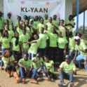 Nigerian alumni wear bright yellow shirts and stand in front of a banner that says KL-YAAN