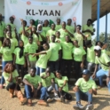 Nigerian alumni wear bright yellow shirts and stand in front of a banner that says KL-YAAN