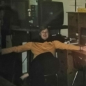 Teacher in a yellow sweater sitting on a chair with his arms wide open.