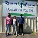 Students stand in front of a sign that reads "Donation Drop Off" 
