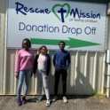 Students stand in front of a sign that reads "Donation Drop Off" 