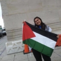 YES student, Saba, standing in front of a concrete building holding up the Palestinian flag.