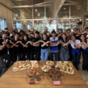 Group of students stand in front of a table with plates of sandwiches and cookies