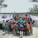 YES alumnus, Mohammad, standing outside with a group of 12 young children. Everyone is wearing masks. 