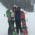 Hiba and a friend holding snowboards and smiling with a snowy hill in the background. 