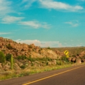 Photo of a long desert road with cactus and sand in the background.