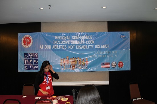 A YES alumna stands in front of a banner that says, "Regional Conference, Inclusive Society"