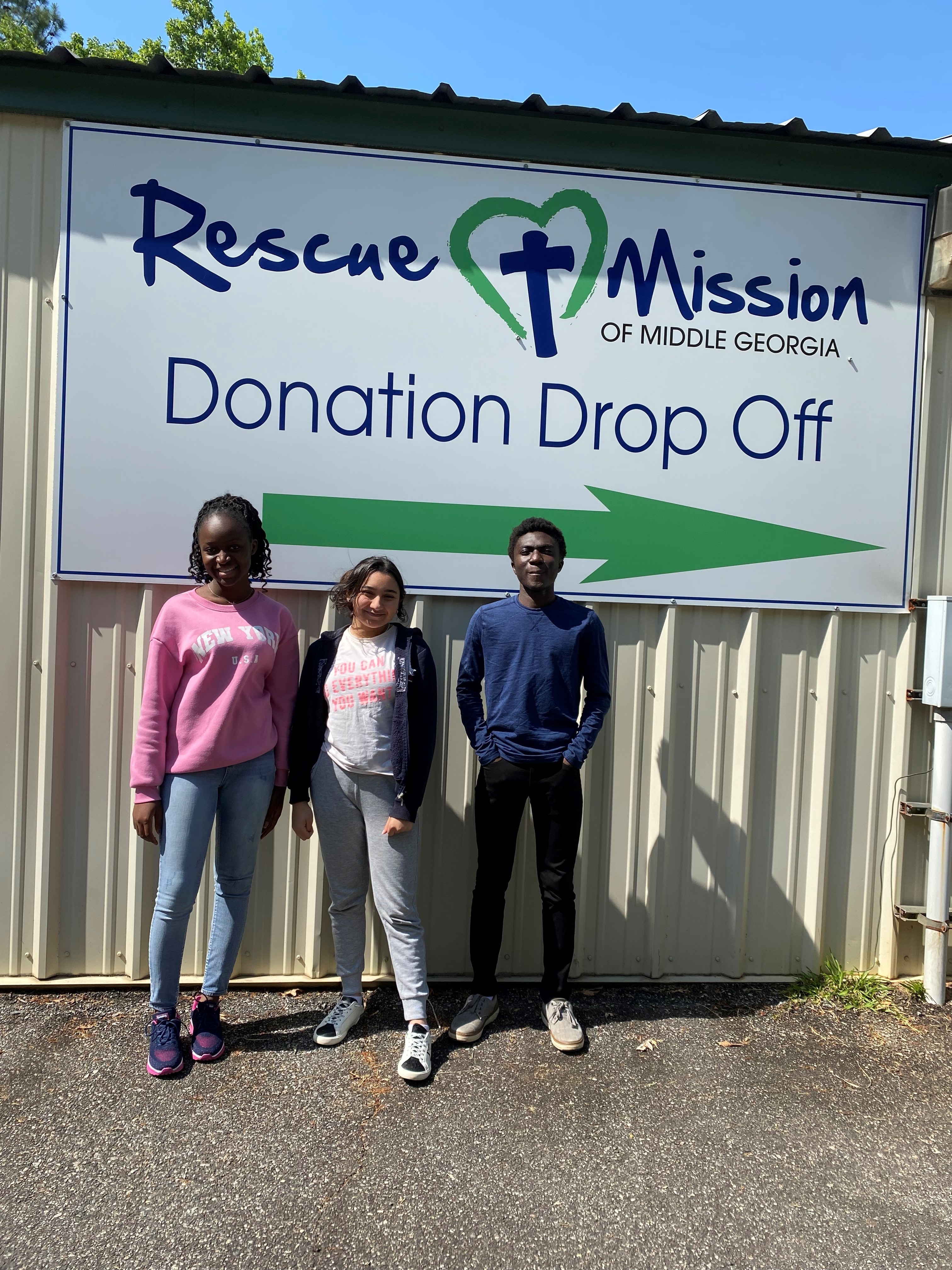 Students stand in front of a sign that reads "Donation Drop Off" 