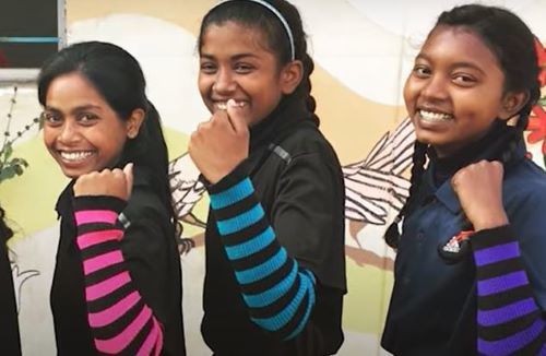 Seema standing with two other girls holding up their fists and smiling to demonstrate "girl power"