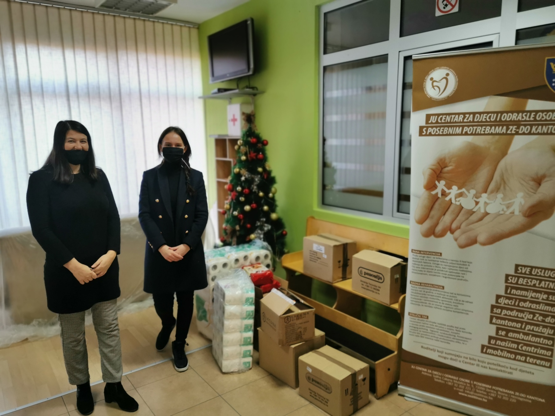 Two women in masks, standing next to piles of donations