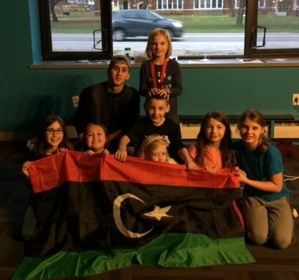 Taha sitting with a group of children in front of the Libyan flag