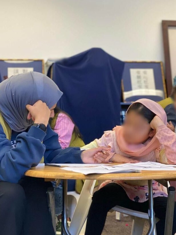 Aljood sits with a young female student helping her study